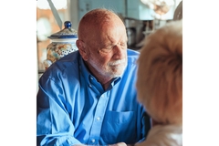 An elderly man looks confused while sitting at a table.